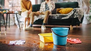 Water leaking from ceiling into bucket causing floor damage inside home