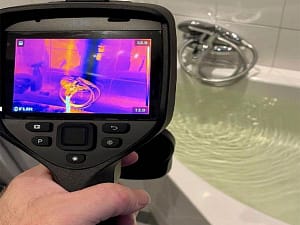 Thermal imaging camera detecting hidden water leak behind wall near bathtub