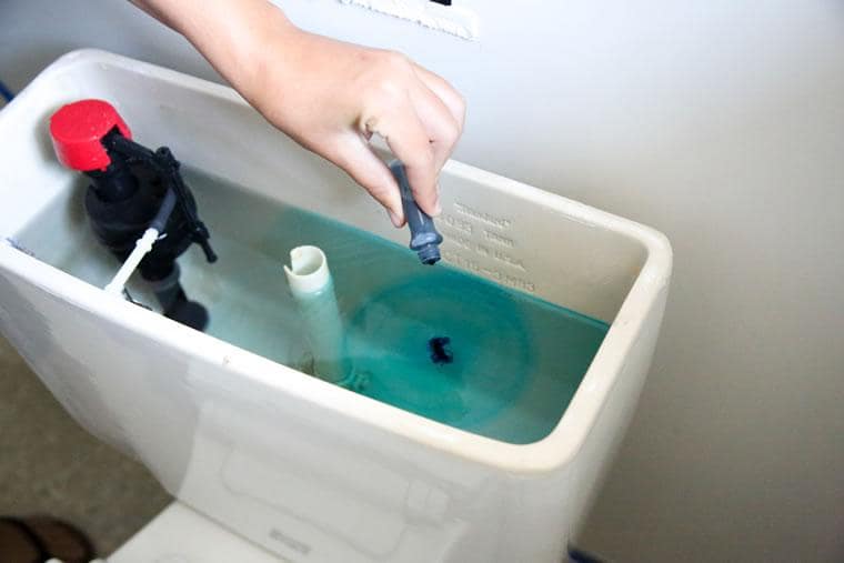 How to Detect Hidden Water Leaks is showing some one searching a toilet tank for hidden leaks.