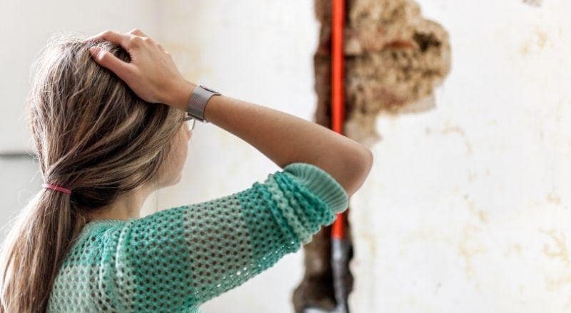 This image is showing someone with their hand on her head while looking at a hidden leak in an open wall.