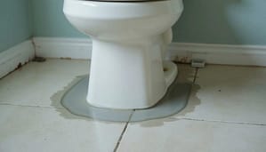 Water leaking from toilet base onto floor indicating failed wax ring