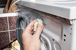 Checking water supply hose connection behind washing machine for hidden leak