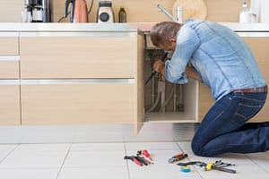 Man checking for hidden water leak under kitchen sink cabinet plumbing