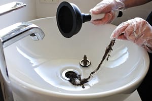Removing hair clog from bathroom sink drain using plunger and hand tool