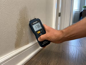 Professional Leak Detection Techniques using a moisture meter pressed against drywall to detect hidden water damage